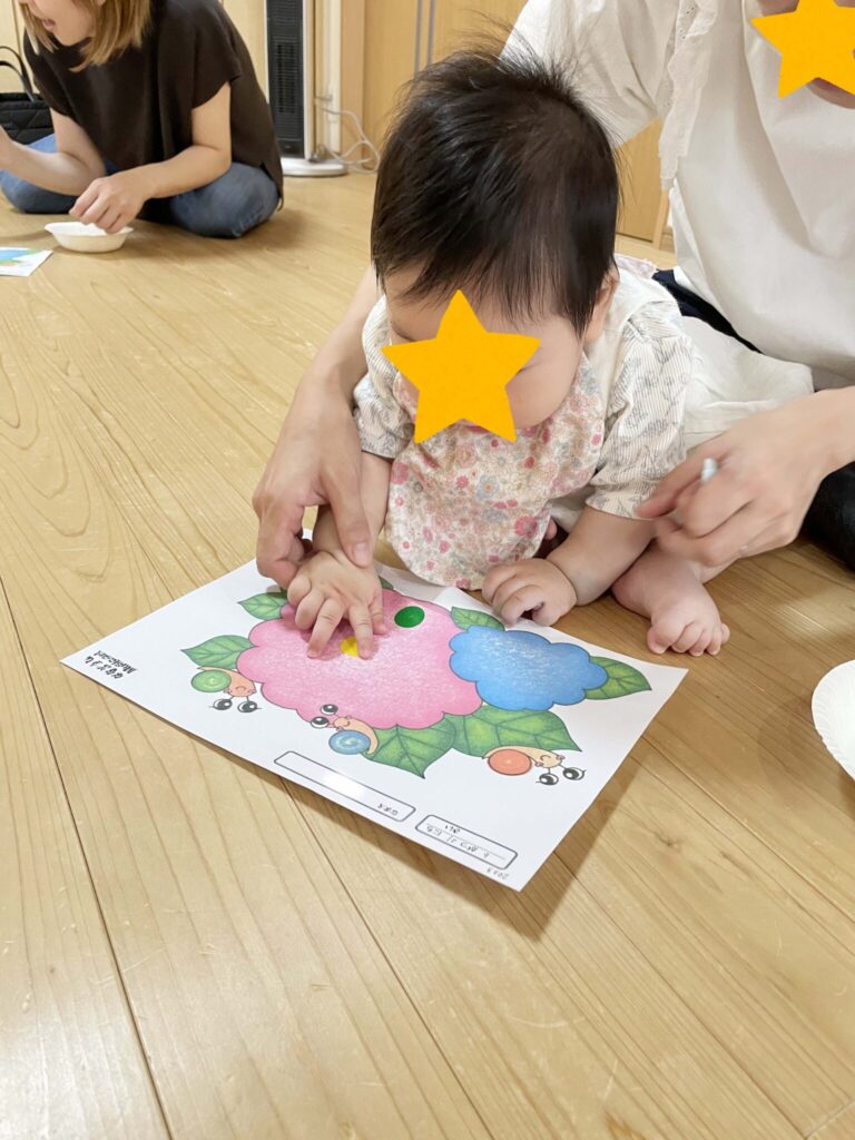 あじさいが描かれた教材にシールを貼る赤ちゃん